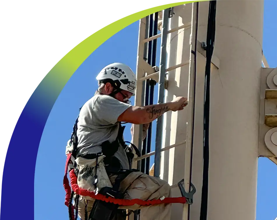 Field technician safely climbing a communication tower during a broadband equipment installation, using full fall protection gear.