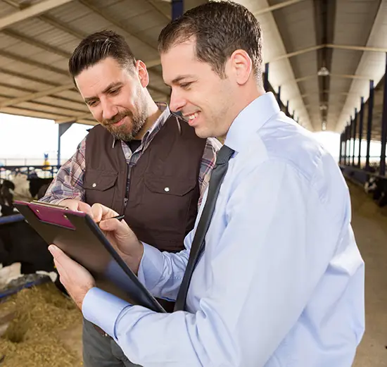 Business professional and farmer reviewing documents on a clipboard inside a modern livestock facility, discussing agricultural operations.